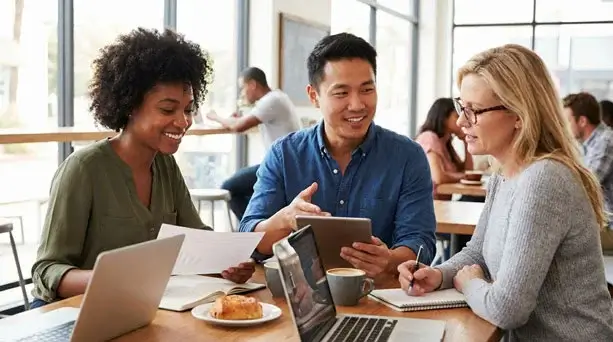 Three consultants collaborating over a tablet and documents at a cafe table, showcasing professional B2B WordPress website design services.