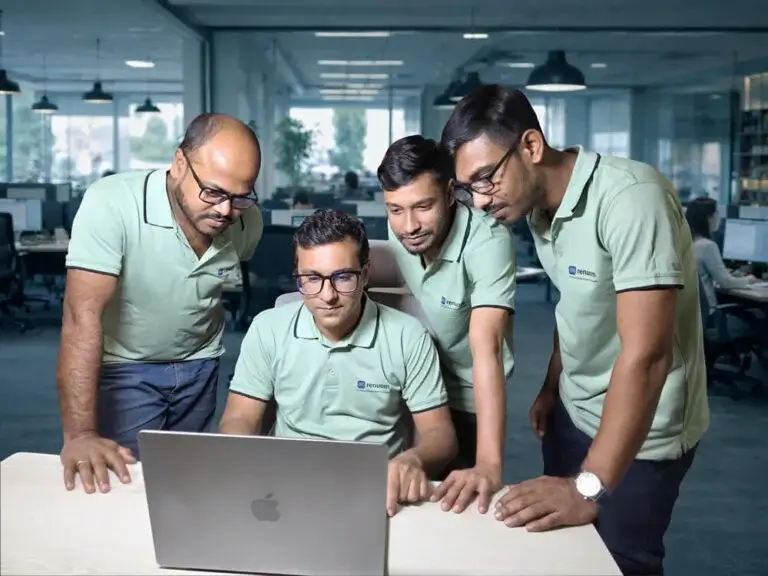 About us: Four Renuom team members collaborating closely around a laptop, showcasing our dedicated web development and video editing experts.